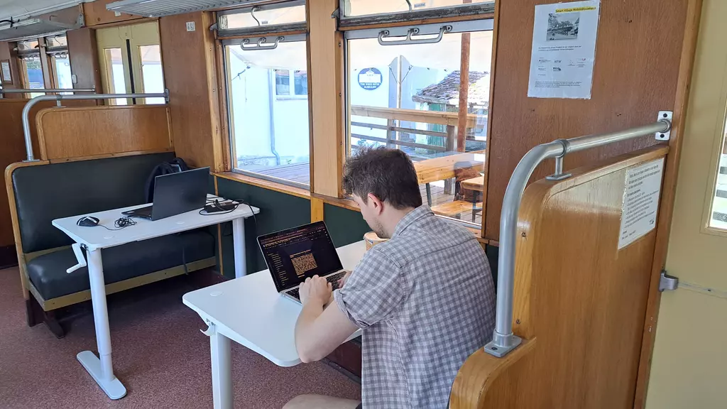 Ein Mann sitzt in einem umgebauten S-Bahn-Wagen an einem Tisch vor seinem Laptop und arbeitet. 