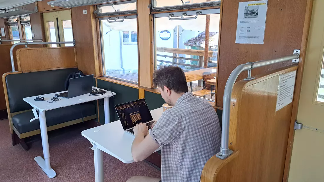 Ein Mann sitzt in einem umgebauten S-Bahn-Wagen an einem Tisch vor seinem Laptop und arbeitet.