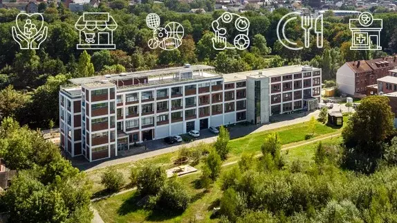 Ein mehrstöckiges Gebäude umgeben von grüner Wiese und einem kleinen Walld