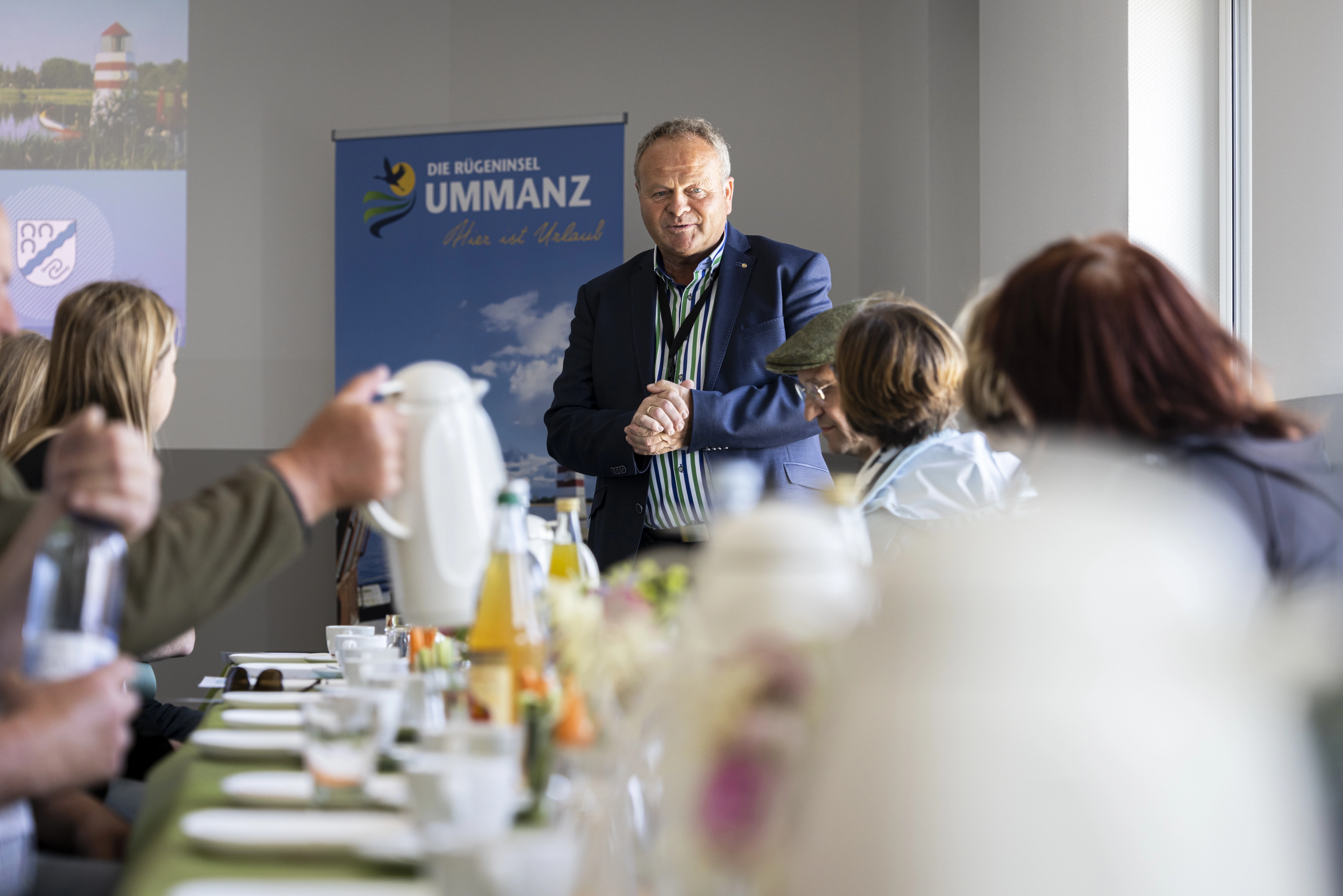 Ein Mann steht am Ende eines Tisches, an dem mehrere Personen sitzen. 