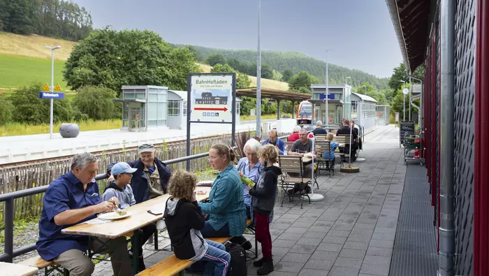 Leute sitzen an einem Tisch vor einem Bahnhof