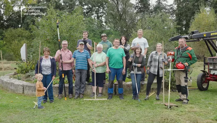 Bewohnerinnen und Bewohner des Dorfes Meinheim stehen mit Gartengeräten auf einer Wiese