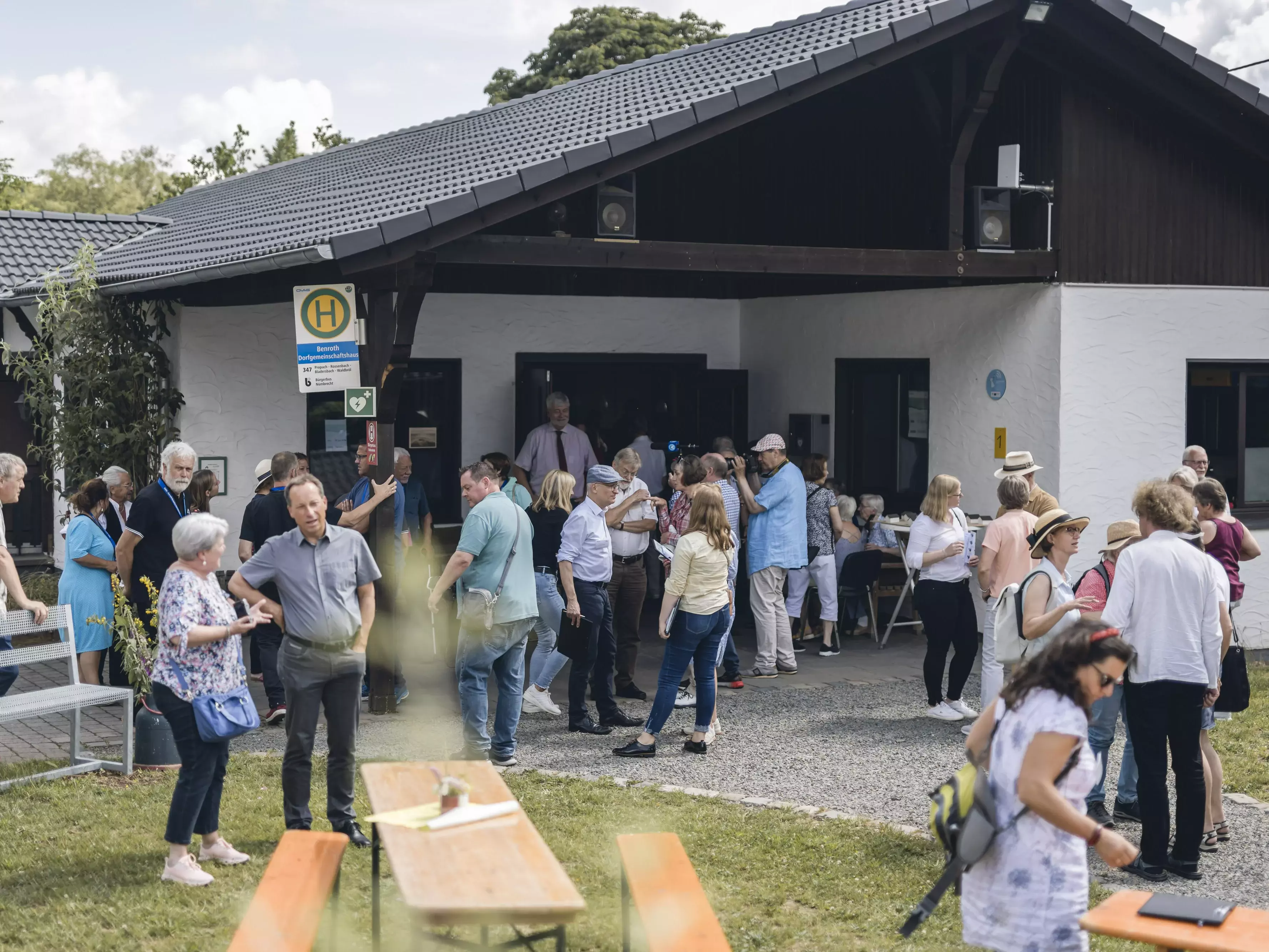 Viele Menschen stehen auf einer Wiese vor einem Haus.