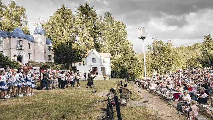 Publikum bei einer Freiluftveranstaltung vor einem Schloss mit einer Bühne davor.