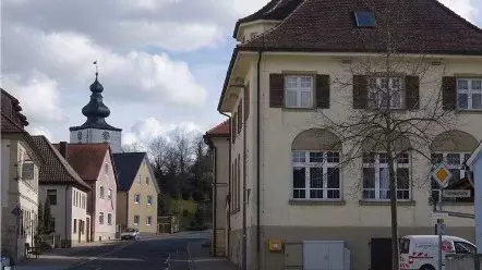 Ein großes leerstehendes altes Gebäude steht rechts am Straßenrand, links kleinere Häuser und eine Kirche. 