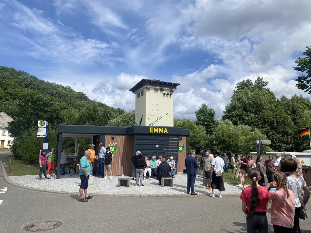 Frauen, Männer und Kinder stehen auf dem Platz vor der eröffneten EMMA in der Sonne. 