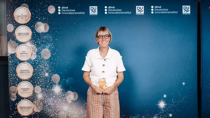 Die Preisträgerin steht auf der Bühne mit ihrer Auszeichnung in der Hand.