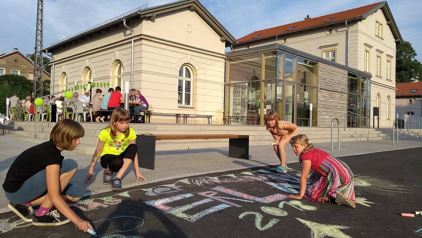 Spielende Kinder malen vor dem Generationenbahnhof Erlau mit Kreide