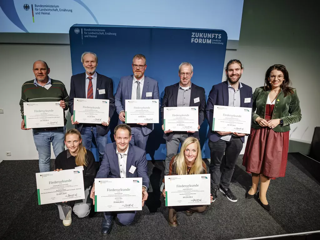 Neun Personen halten ihre Förderbescheide in die Kamera.