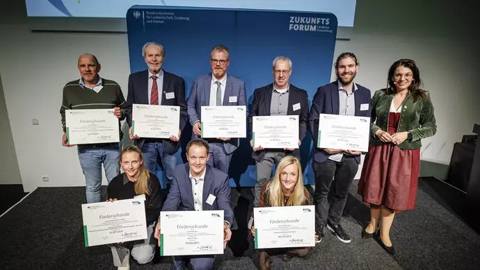 Neun Personen halten ihre Förderbescheide in die Kamera.