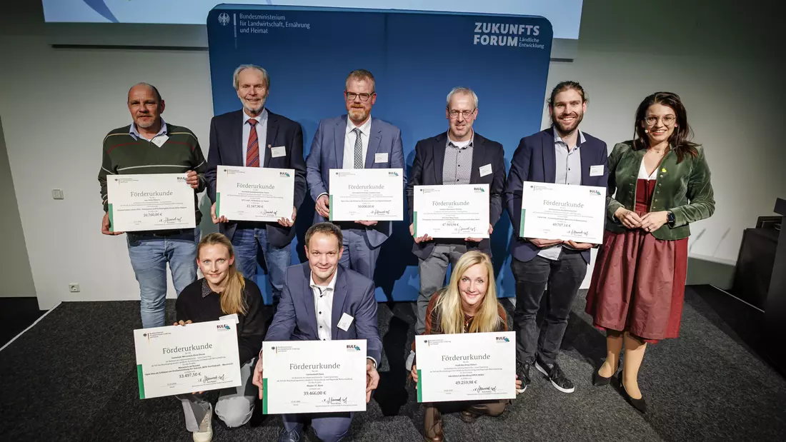 Neun Personen halten ihre Förderbescheide in die Kamera.