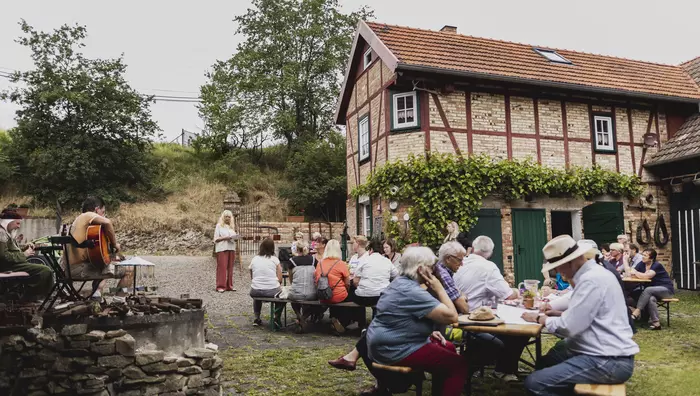 Menschen sitzen auf Bierbänken vor einem Fachwerkhaus.