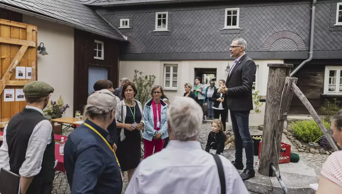 Ein Mann spricht auf einem Brunnen in einem Innenhof zu einer Gruppe von Menschen.