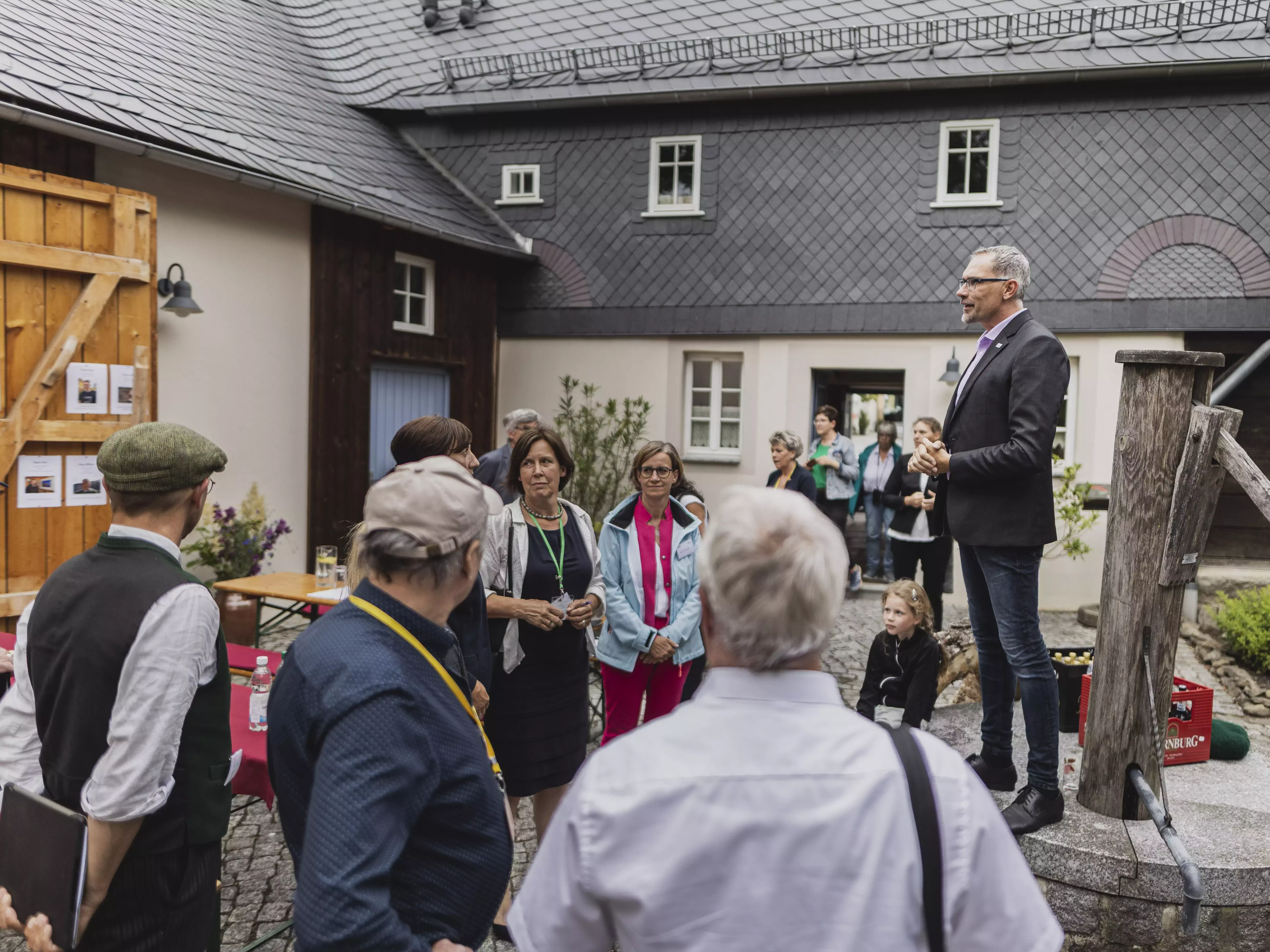 Ein Mann spricht auf einem Brunnen in einem Innenhof zu einer Gruppe von Menschen.