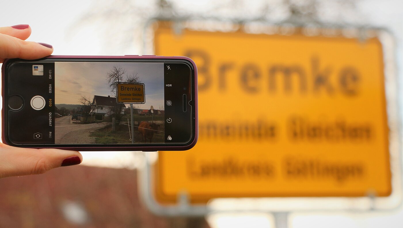 Bildschirm eines Mobiltelefons, mit dem das Ortseingangsschild von Bremke fotografiert wird.  