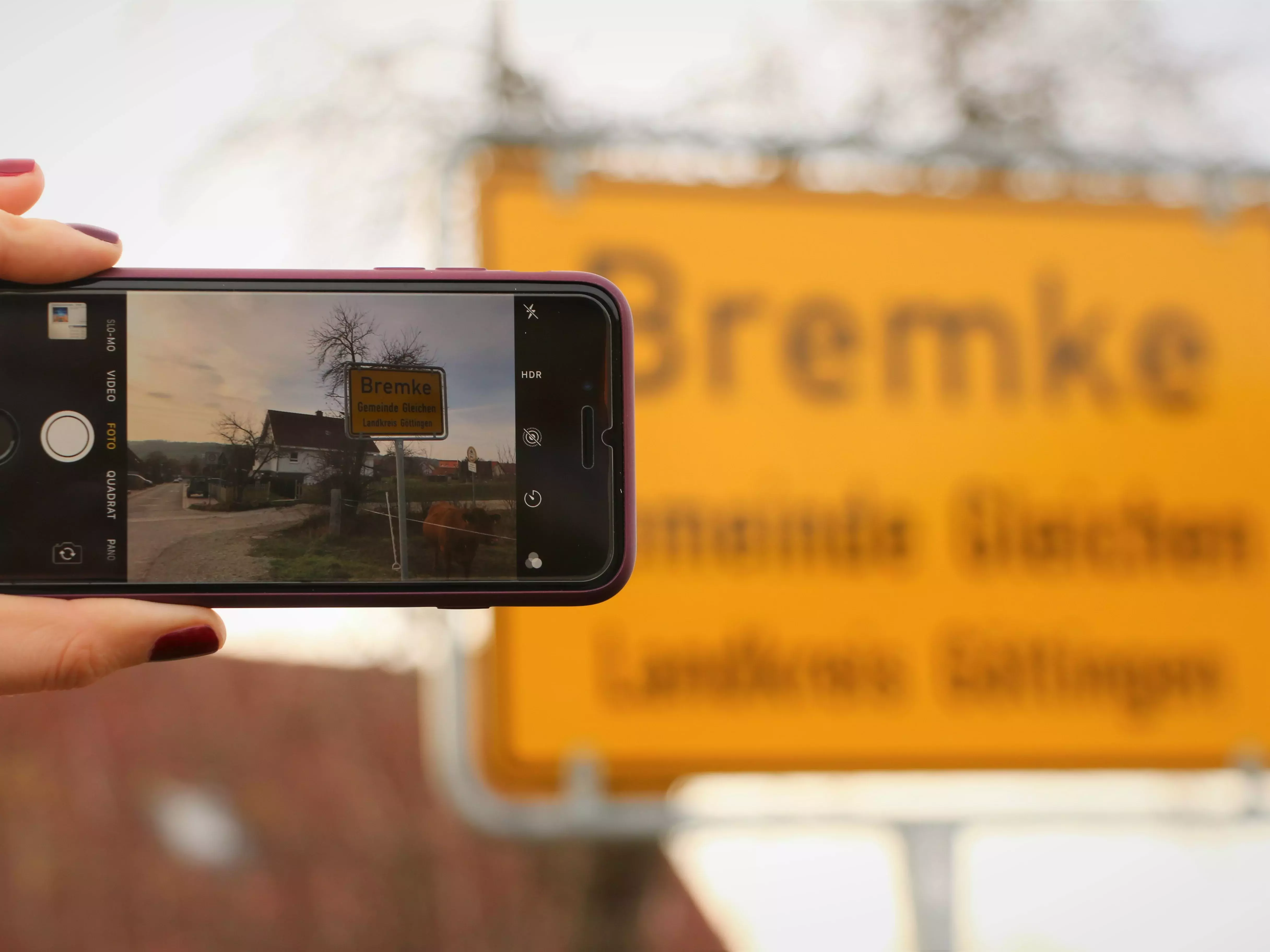 Bildschirm eines Mobiltelefons, mit dem das Ortseingangsschild von Bremke fotografiert wird.  
