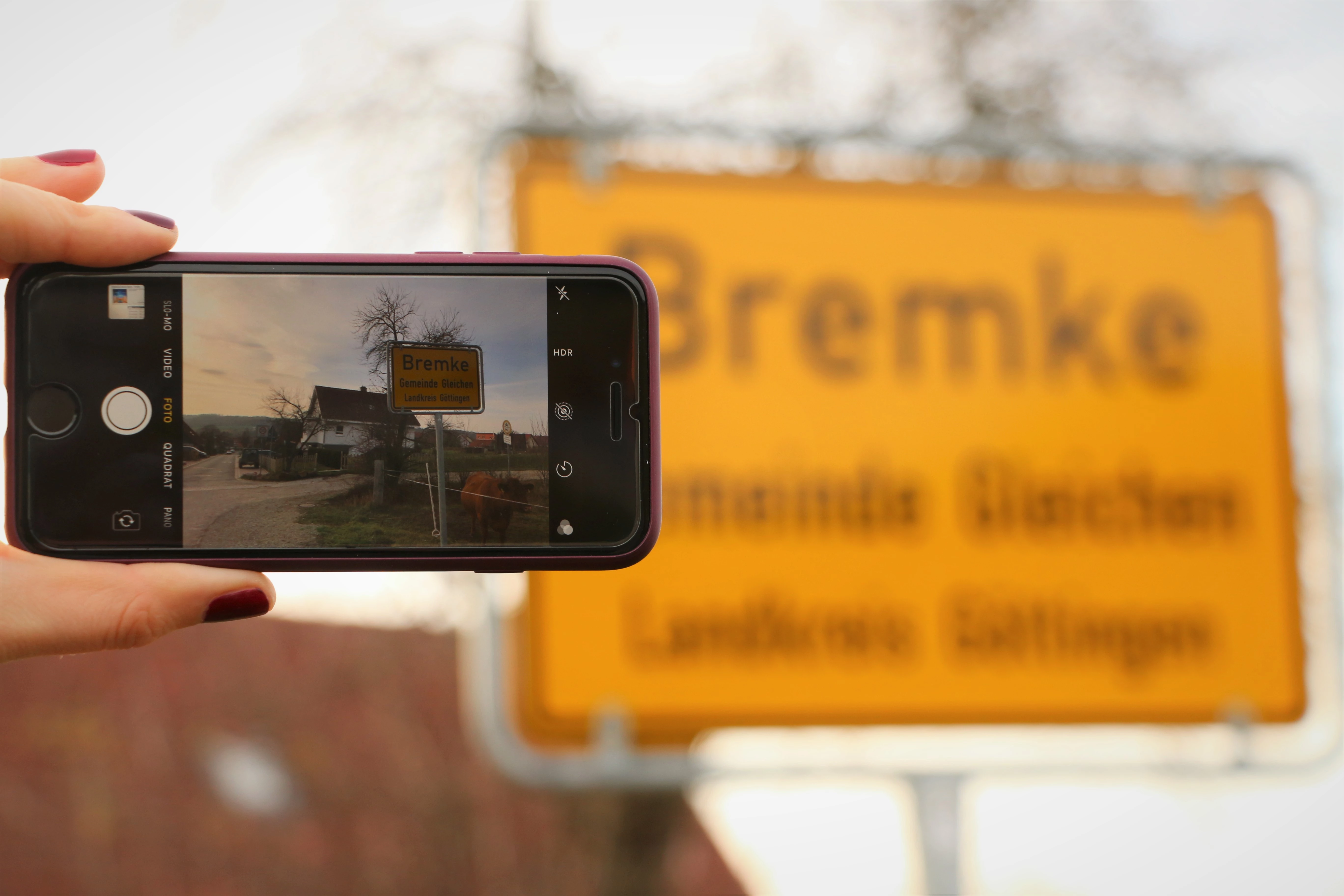Bildschirm eines Mobiltelefons, mit dem das Ortseingangsschild von Bremke fotografiert wird.  