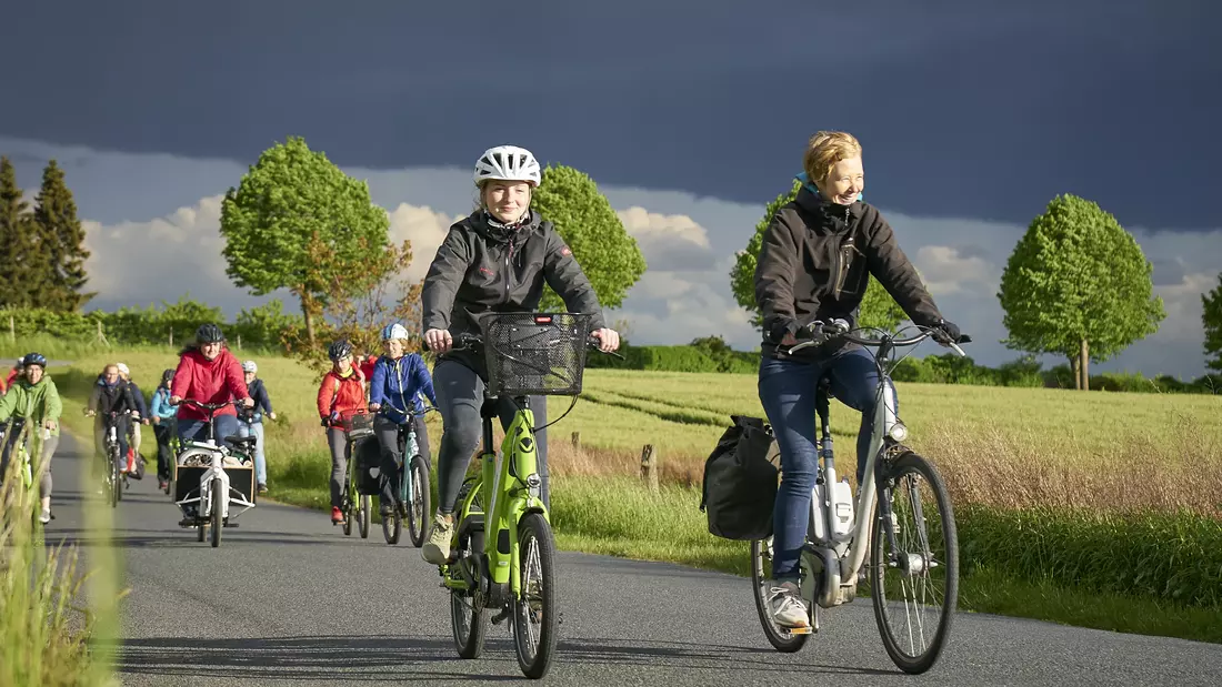 Mehrere Radfahrerinnen sind auf einer Landstraße im Sonnenschein unterwegs.