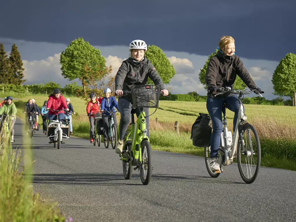 Mehrere Radfahrerinnen sind auf einer Landstraße im Sonnenschein unterwegs.