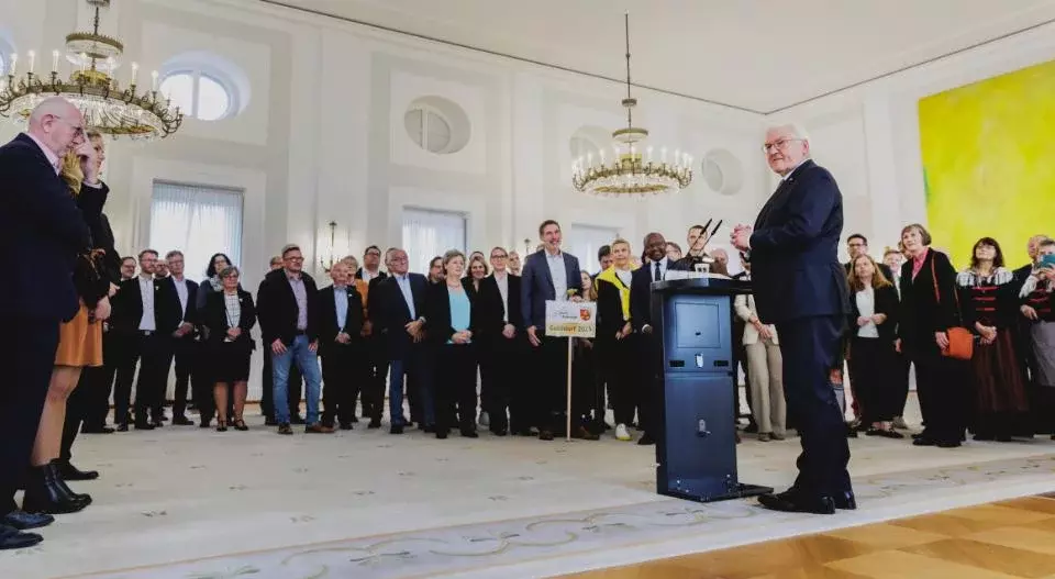 Sieger des Dorfwettbewerbs stehen in einem Saal des Schlosses Bellevue, Bundespräsident Frank-Walter Steinmeier am Rednerpult.