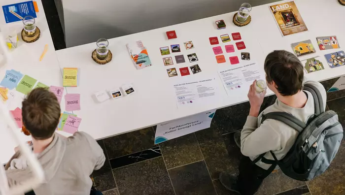 2 Personen betrachten Materialien, die auf einem Tisch ausgelegt sind.