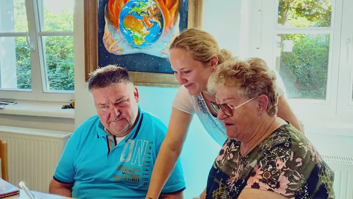 Eine junge Frau erläutert einer Seniorin und einem Senior etwas am Mobiltelefon.