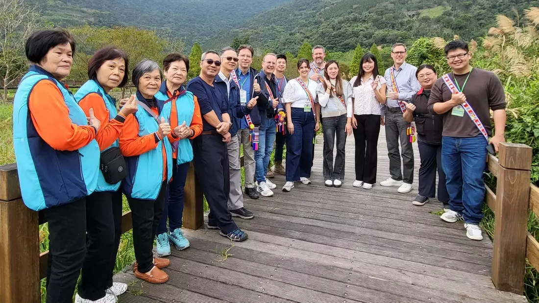 Eine Gruppe Frauen und Männer steht auf einem Holzsteg vor bewaldeten Hügeln.n.