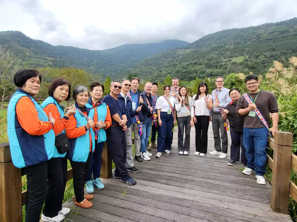 Eine Gruppe Frauen und Männer steht auf einem Holzsteg vor bewaldeten Hügeln.n.