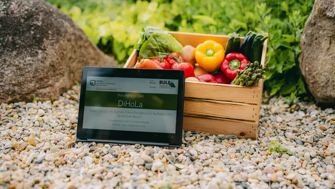 Ein Tablet lehnt an einer Holzkiste voller Gemüse.