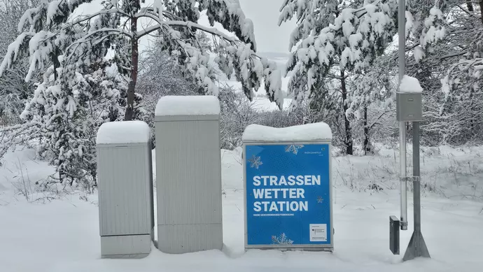 Mehrere Messstationen stehen vor verschneiten Bäumen.