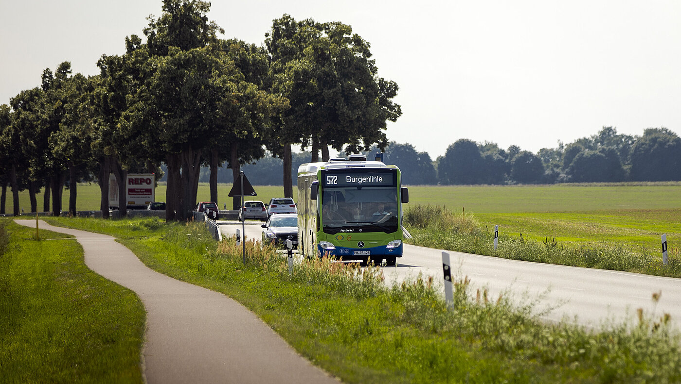 Ein Bus fährt über eine Landstraße, daneben verläuft ein Fahrradweg