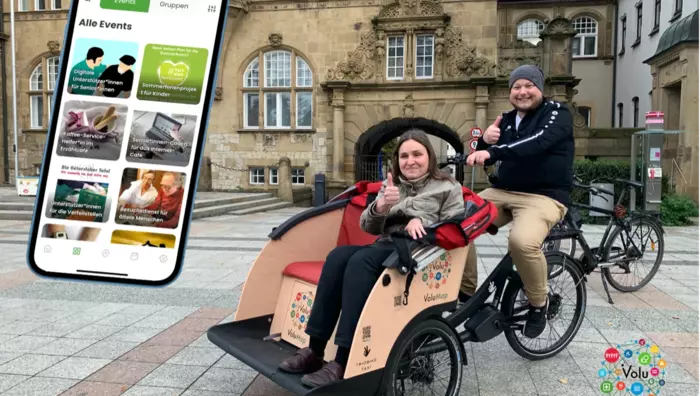 Eine junger Mann und eine junge Frau auf dem VoluMap-Lastenrad sowie die Ansicht der VoluMap-App auf dem Bildschirm eines Mobiltelefons