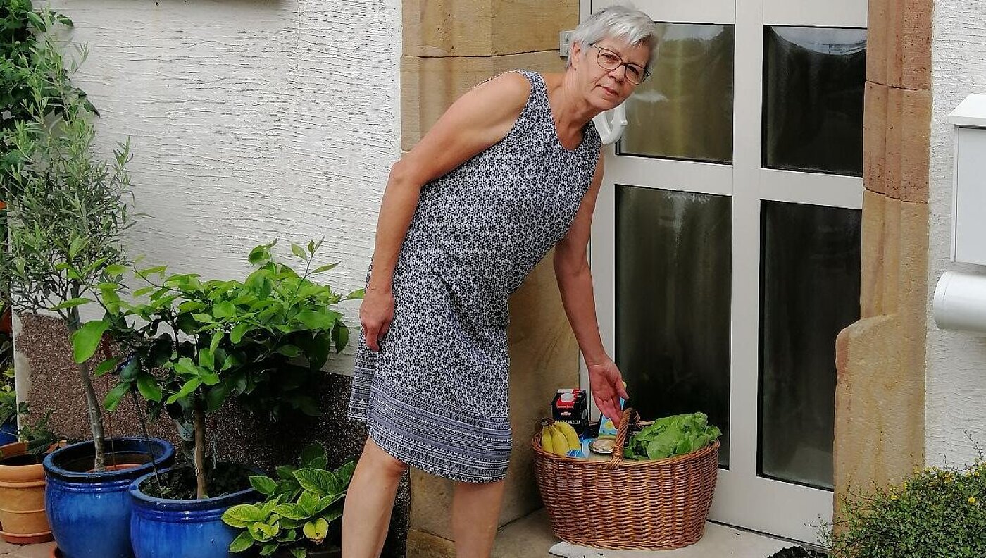 Eine Frau stellt einen Korb mit Lebensmitteln vor einer Haustür ab